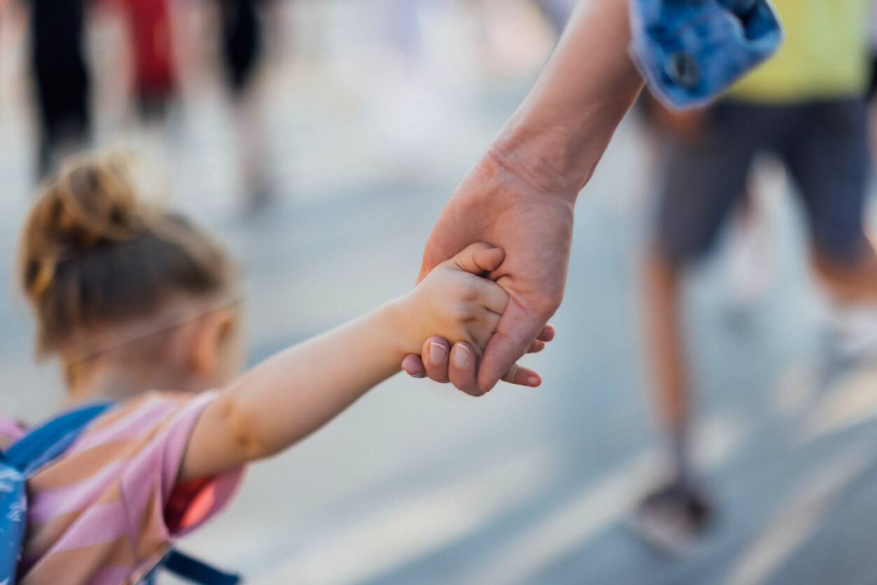 Close up photo of little girl with backpack holding a mom hand while walking to the school together.
