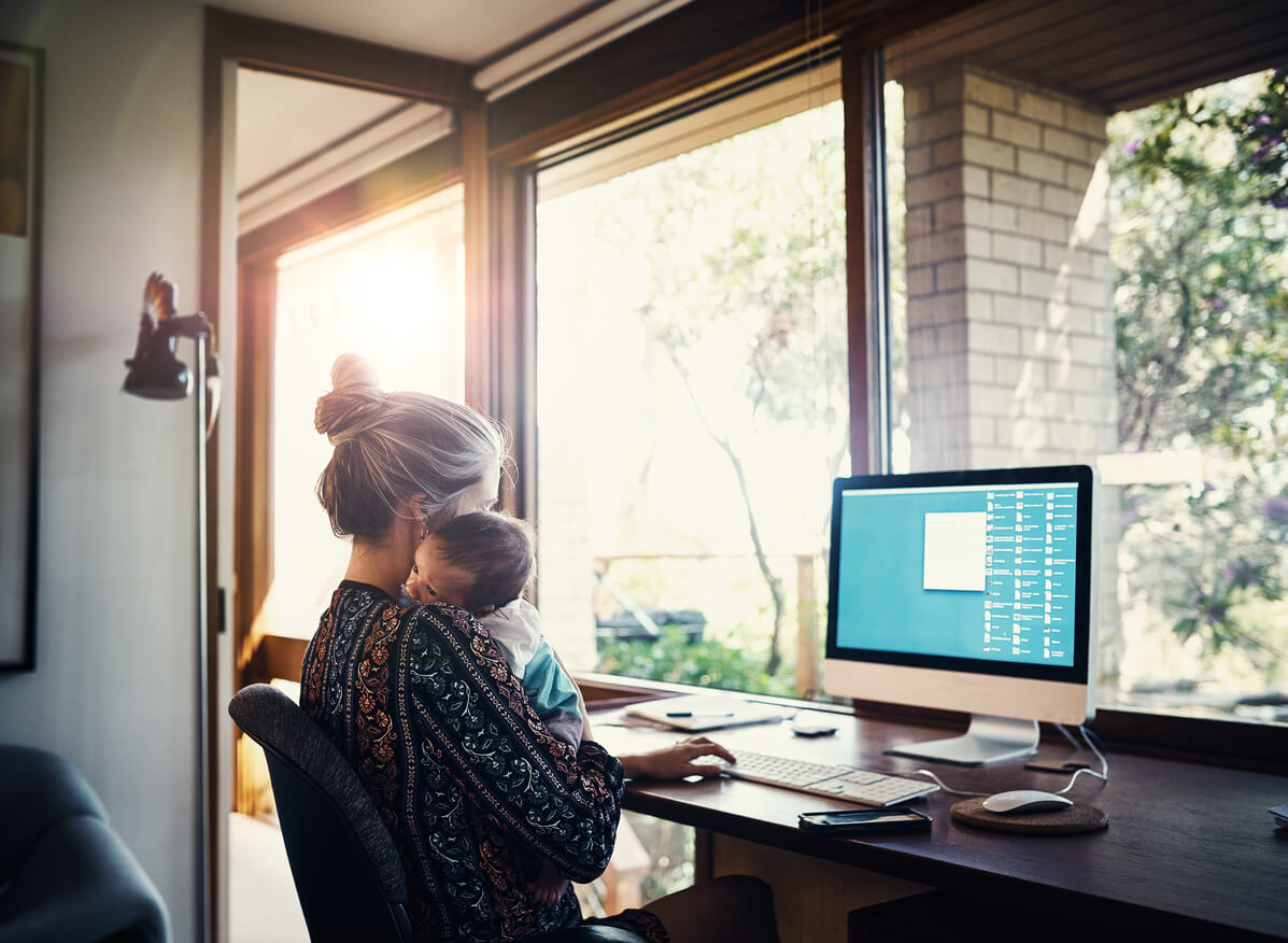 Shot of a young woman working at home while holding her newborn baby son